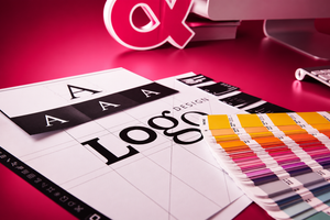 Color swatch book and logo design paper on a pink surface with a logo in the background.
